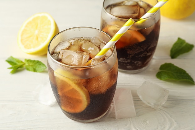 Glasses with cold cola and citrus on white cement background