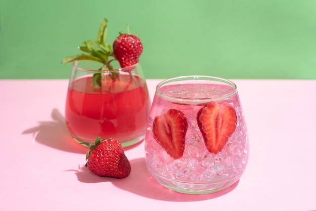 Glasses with functional water, strawberry lemonade with ice cubes on green and pink background, summer drinks concept, close up.