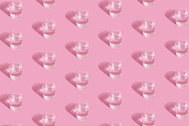 Glasses with water and shadow pattern on pink background