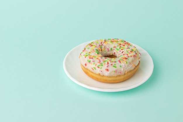 Glazed donut on a white plate on a blue surface