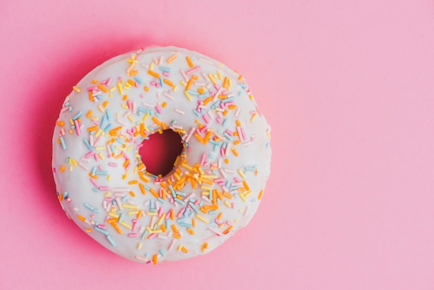 Glazed donut with sprinkles on pink backdrop