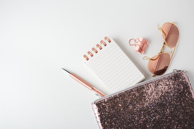 Glitter bag with pen, notepad and sunglasses on white background