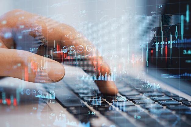 Global economy and market growth concept with digital candlestick and financial chart indicators on human fingers typing on laptop keyboard double exposure