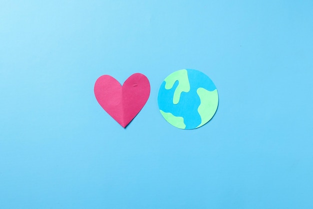 Globe and red heart shape made from paper isolated on blue background. World earth day concept.