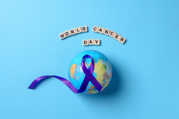 Globes with purple ribbon cancer awareness with word world cancer day on blue background