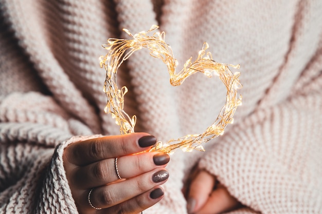 Photo gloglowing heart in the hands of a woman. happy valentine's day. plaid, comfort, winter, garlandwing heart in the hands of a woman. happy valentine's day