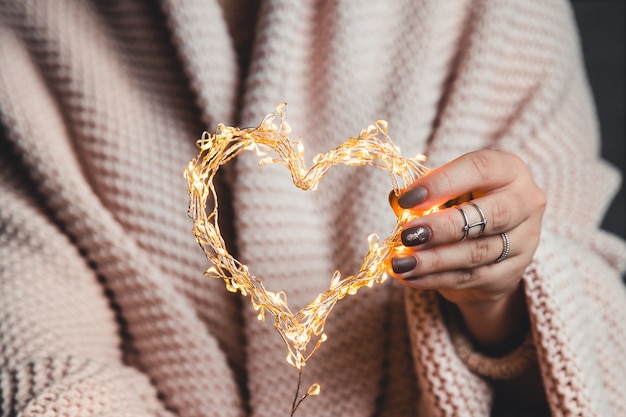 Photo gloglowing heart in the hands of a woman. happy valentine's day. plaid, comfort, winter, garlandwing heart in the hands of a woman. happy valentine's day