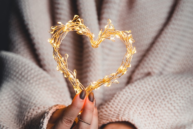 Gloglowing heart in the hands of a woman. Happy Valentine's day. Plaid, comfort, winter, garlandwing heart in the hands of a woman. Happy Valentine's day