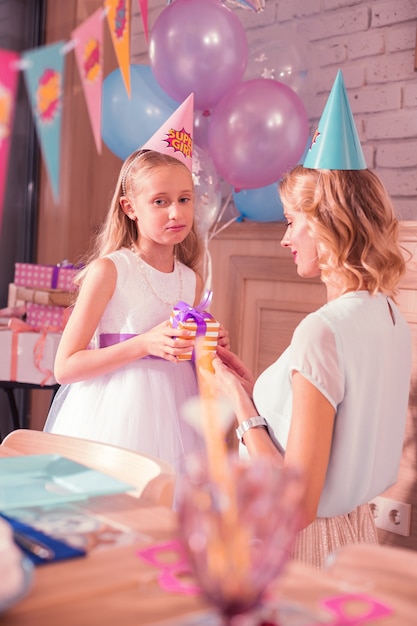 Gloomy mood. Calm young woman sitting next to her daughter and the girl feeling gloomy at her birthday party