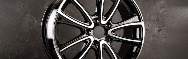 Glossy black alloy wheels fragment on a textured black background