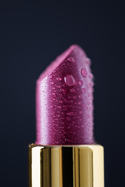 Glossy pink lipstick with water drops on black background.