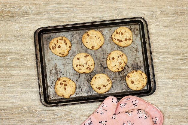 Photo a glove cook with tray of homemade chocolate chip cookies on wood table