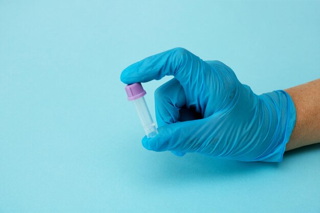 A gloved hand holds an empty test tube on a blue background with copy space modern diagnostics