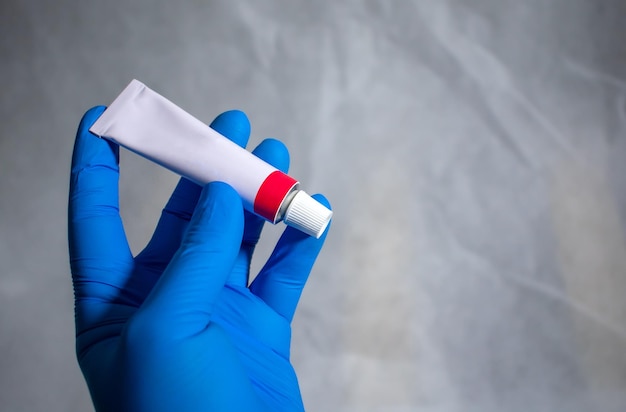 The gloved hand holds and presents a closed tube of medical ointment. medical advertising concept