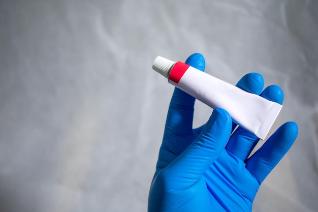 The gloved hand holds and presents a closed tube of medical ointment. medical advertising concept