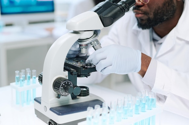 Gloved hands of african american male scientist studying new virus in microscope