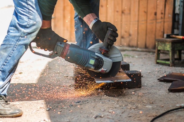 A gloved worker cuts a metal sheet with an angle grinder Sparks fly from the grinding wheel