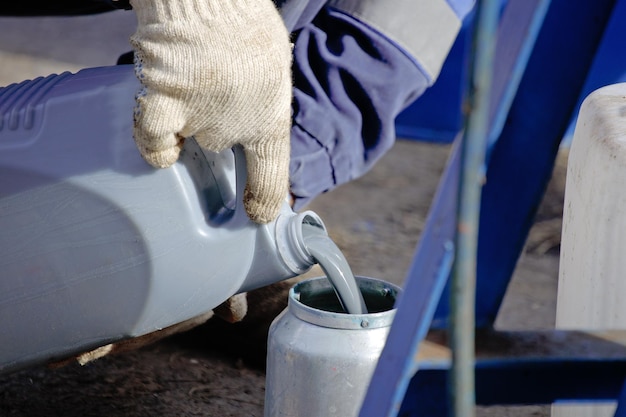 A gloved worker pours gray paint from a canister into a spray gun