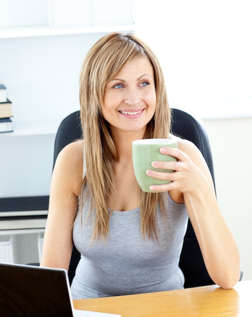 Glowing businesswoman holding a cup using her laptop 