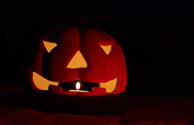 A glowing carved pumpkin with a candle inside in a dark background - halloween concept