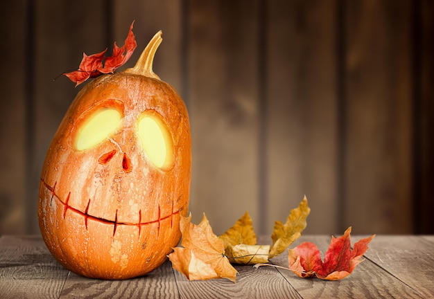 Glowing Halloween pumpkin Jackolantern and autumn leaves on wooden backgroun