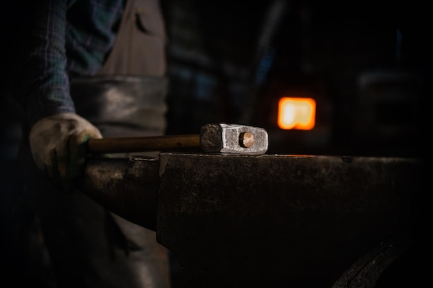 Glowing hammer on the anvil in workshop  a man worker standing on the background