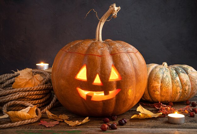 A glowing pumpkin lantern Jacks head on a background of foliage berries and candles