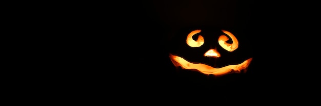 Photo glowing smiling face halloween pumpkin, candle holder, isolated on night dark black background. space for text.