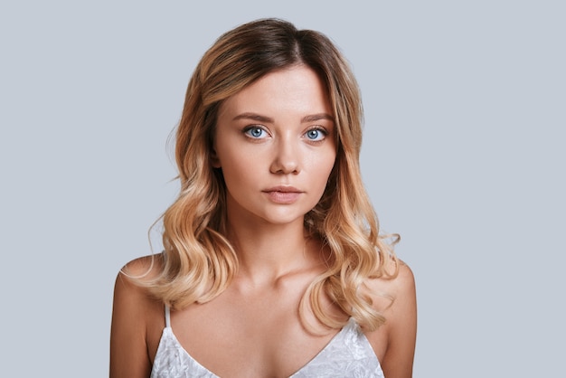 Glowing with natural beauty. Attractive young woman looking at camera while standing against grey background