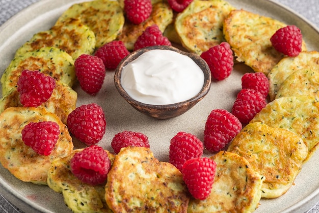 Gluten-free zucchini pancakes with fresh raspberries, raspberry jam, sour cream on a grey plate