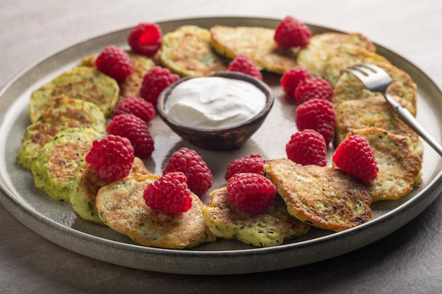 Gluten-free zucchini pancakes with fresh raspberries, raspberry jam, sour cream on a grey plate