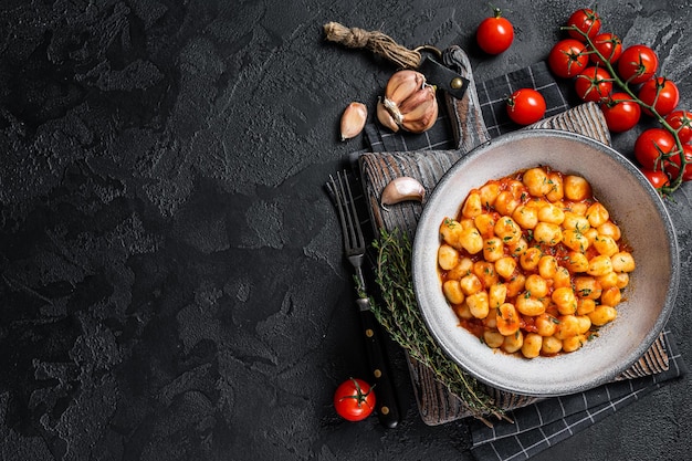 Gnocchi potato pasta with tomato sauce and thyme. Black background. Top view. Copy space.