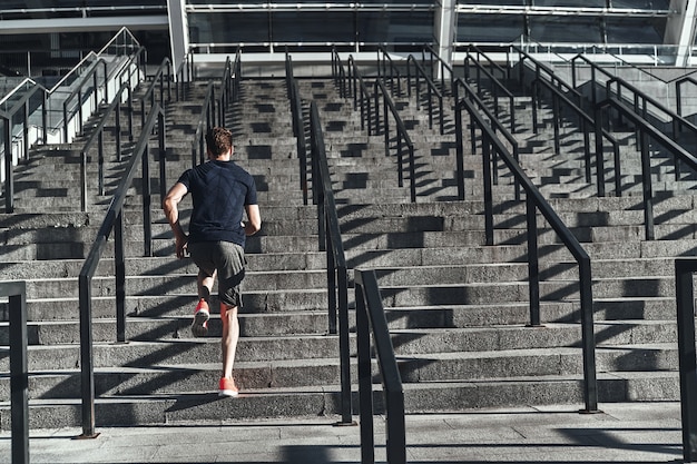 Go! Full length rear view of young man in sports clothing running up the stairs 