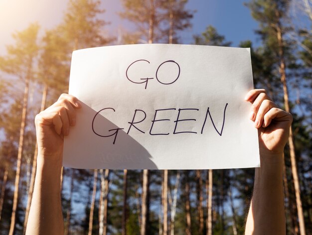 Go green words written on paper poster in male hands in forest.