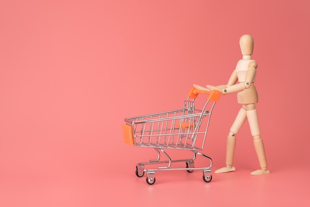 Go shopping concept. Photo of wooden mannequin pushing card on wheels isolated pastel light color backdrop