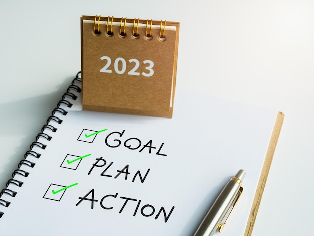 Goal plan and action text with checkmarks on notepad with pen and small beige desk calendar on white background Business motivation resolution inspiration concepts