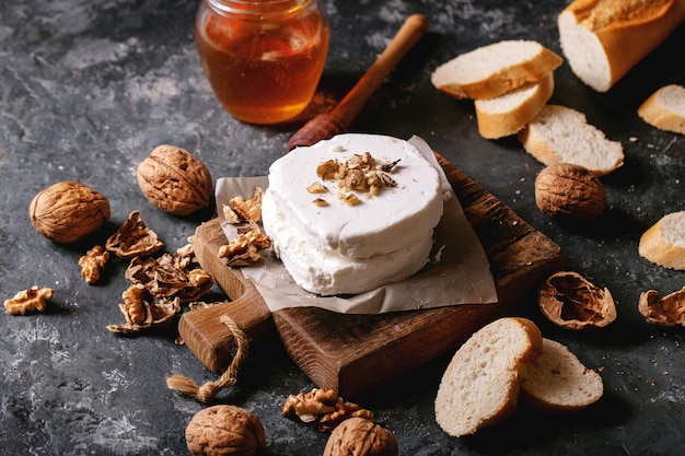 Goat cheese served with honey and walnuts over dark texture background. Copy space