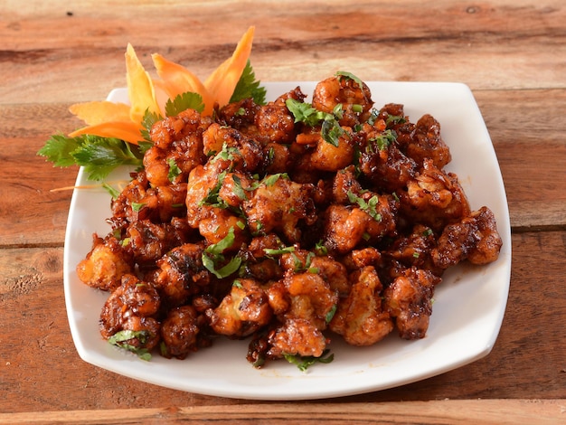 Gobi Manchurian Popular indochinese food made of cauliflower florets served in a white plate over a rustic wooden table selective focus