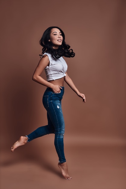 Going crazy. Full length of beautiful young woman smiling and looking at camera while hovering against brown background