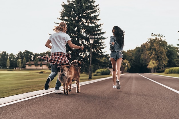 Going crazy together. Full length rear view of beautiful young couple running with their dog while spending time outdoors