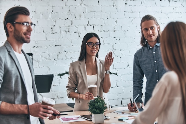 Going over details. Group of young modern people in smart casual wear discussing business while standing in the creative office