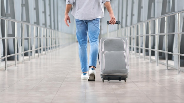 Going to plane male traveller walking with suitcase in airport terminal rear view with free space