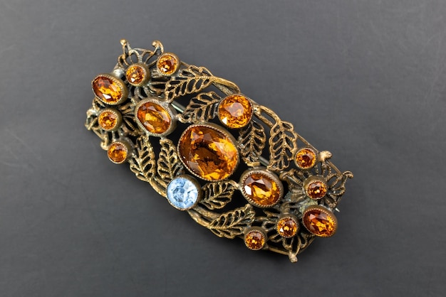 a gold brooch with a blue and white flower on it is surrounded by leaves and branches