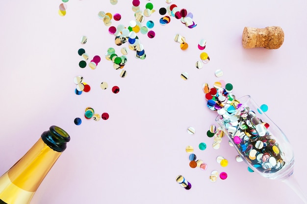 Gold champagne bottle and glasses with confetti on a pink background