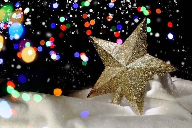 Gold Christmas star in the snow. Defocused lights in the background. Decoration for the Christmas tree. Christmas background