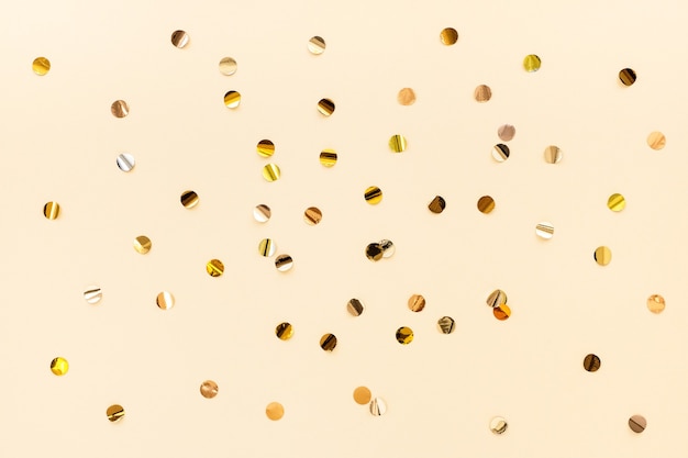 Gold confetti scattered on a beige background, top view. Color trend 2021, set sail champagne. Festive minimalistic background.