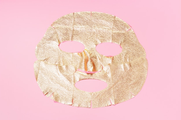 Gold fabric mask on a pink background close-up, skin hydration concept.