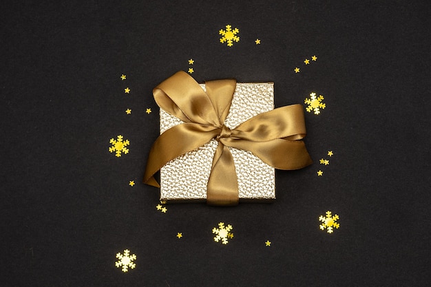 Gold gift box with ribbon and sparkling decorations on black