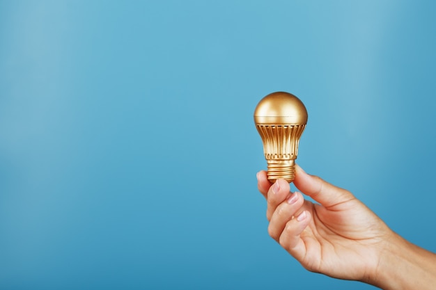 Gold light bulb in hand on a blue background as a concept of ideas and assistance