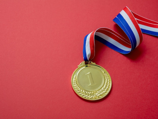 Gold medal Champion trophy award and ribbon Prize in sport for winner isolated on red background